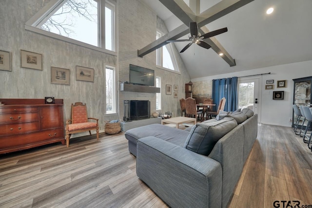 living room with a large fireplace, high vaulted ceiling, wood finished floors, and a ceiling fan