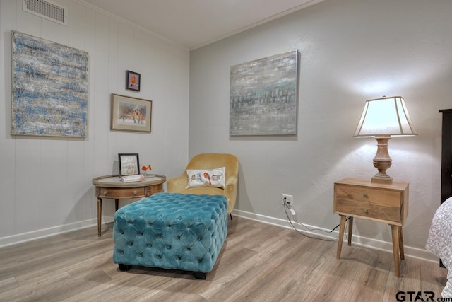 living area with baseboards, wood finished floors, visible vents, and ornamental molding