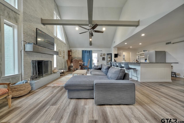 living area featuring light wood-type flooring, beamed ceiling, high vaulted ceiling, visible vents, and a brick fireplace