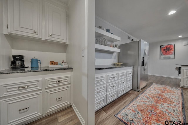 kitchen featuring light wood-type flooring, stainless steel refrigerator with ice dispenser, dark stone countertops, open shelves, and white cabinetry