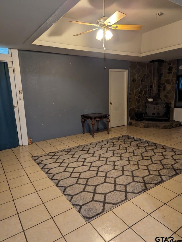 basement featuring a wood stove, ceiling fan, and tile patterned floors