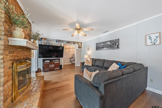 living area with visible vents, wood finished floors, ceiling fan, a fireplace, and ornamental molding