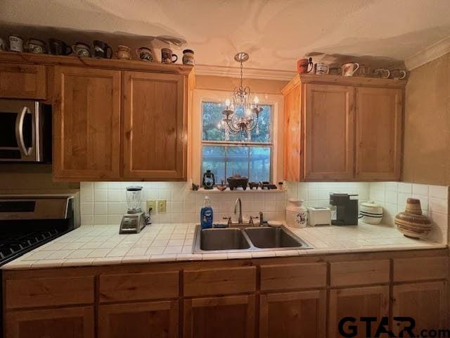 kitchen featuring black range oven, tile counters, sink, ornamental molding, and a notable chandelier