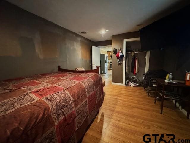 bedroom featuring stainless steel fridge and light wood-type flooring