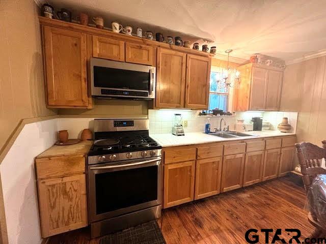 kitchen with ornamental molding, stainless steel appliances, dark wood-type flooring, sink, and decorative light fixtures