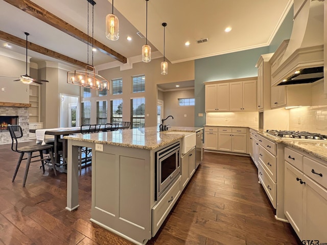 kitchen with stainless steel appliances, premium range hood, hanging light fixtures, and a center island with sink