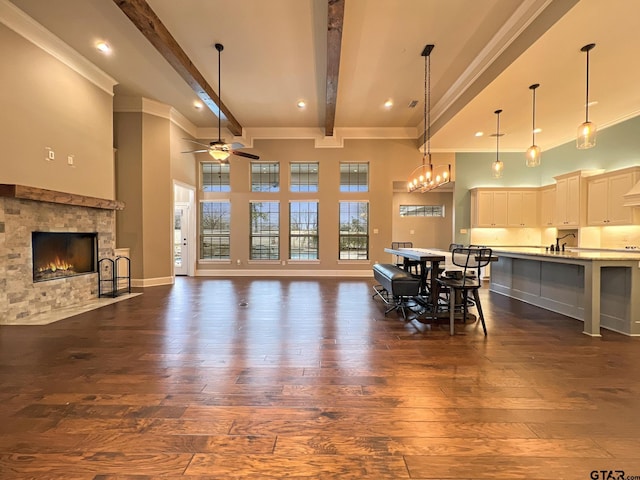 dining area with a high ceiling, a tile fireplace, ceiling fan with notable chandelier, and beam ceiling