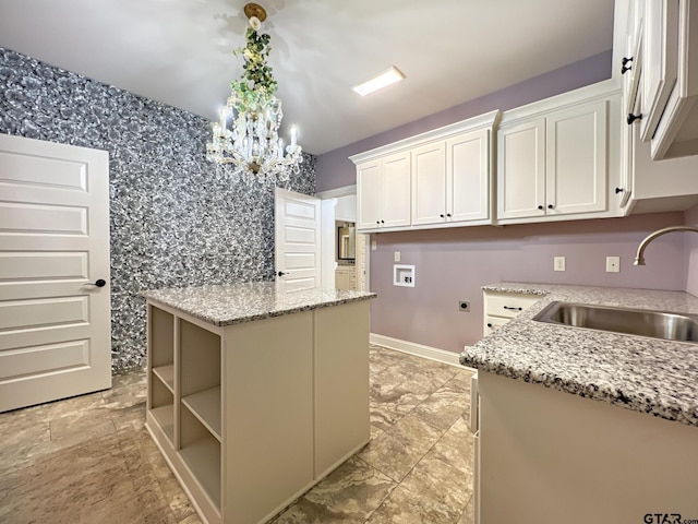 kitchen featuring light stone countertops, sink, white cabinets, and decorative light fixtures