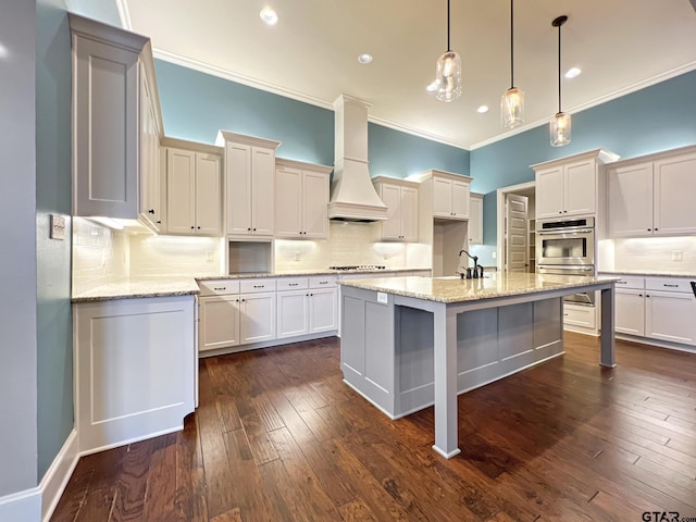 kitchen with tasteful backsplash, gas cooktop, custom range hood, stainless steel double oven, and a kitchen island with sink