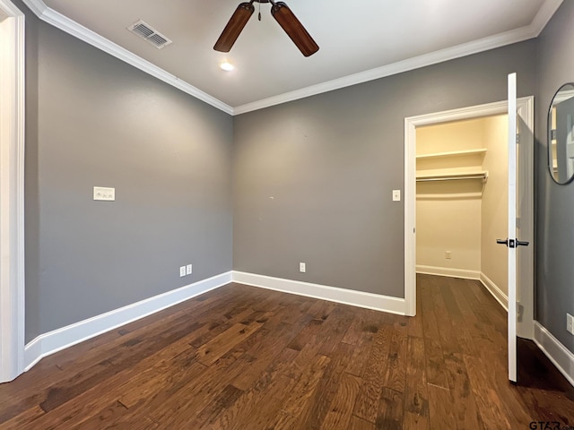 unfurnished bedroom featuring dark wood-type flooring, crown molding, a spacious closet, a closet, and ceiling fan