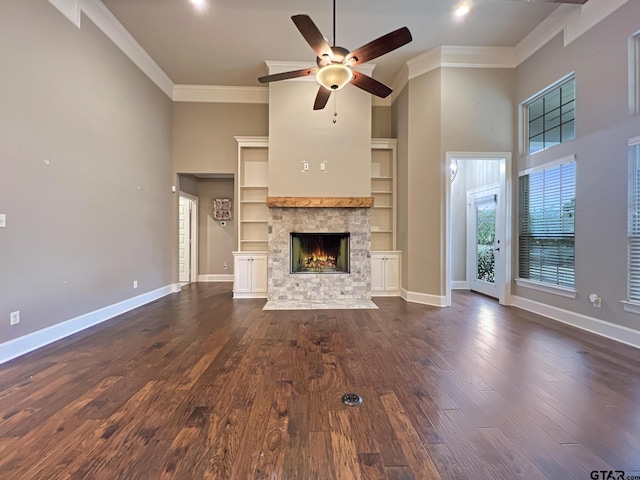 unfurnished living room with built in features, a fireplace, ceiling fan, crown molding, and dark wood-type flooring