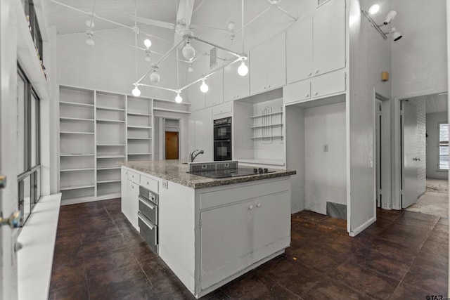 kitchen with open shelves, a towering ceiling, white cabinets, an island with sink, and black appliances