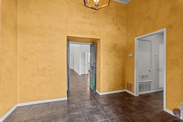 tiled empty room featuring baseboards, a high ceiling, and visible vents