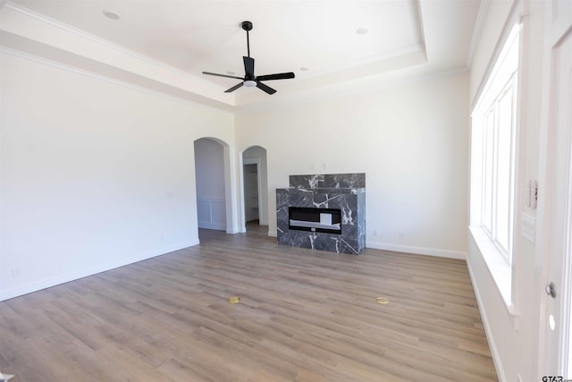 unfurnished living room featuring ornamental molding, a raised ceiling, a premium fireplace, light hardwood / wood-style floors, and ceiling fan