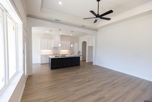 kitchen with an island with sink, hardwood / wood-style flooring, white cabinetry, and crown molding