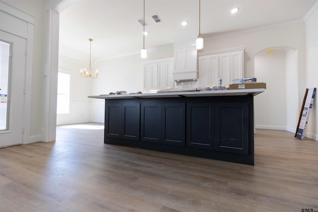 kitchen with wood-type flooring, a center island with sink, crown molding, pendant lighting, and white cabinets