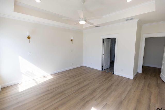 empty room featuring ceiling fan, wood-type flooring, ornamental molding, and a raised ceiling