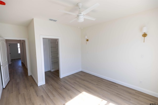 unfurnished bedroom featuring ceiling fan, a closet, light wood-type flooring, and a walk in closet