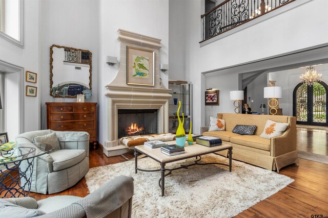 living room featuring hardwood / wood-style floors, a towering ceiling, a large fireplace, and french doors