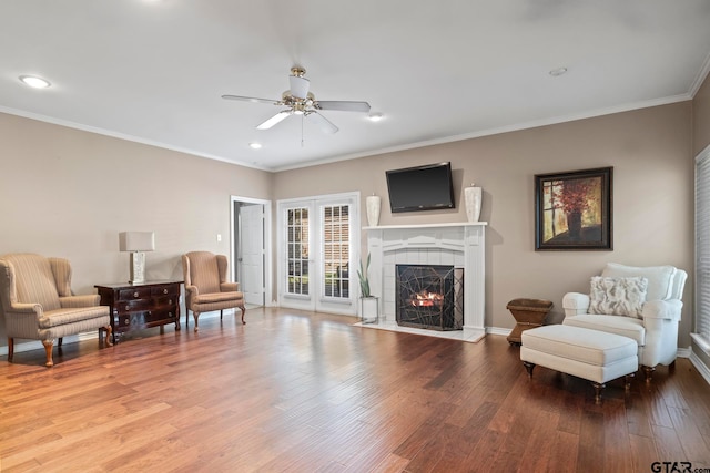 living area with wood-type flooring, a tile fireplace, ceiling fan, and crown molding