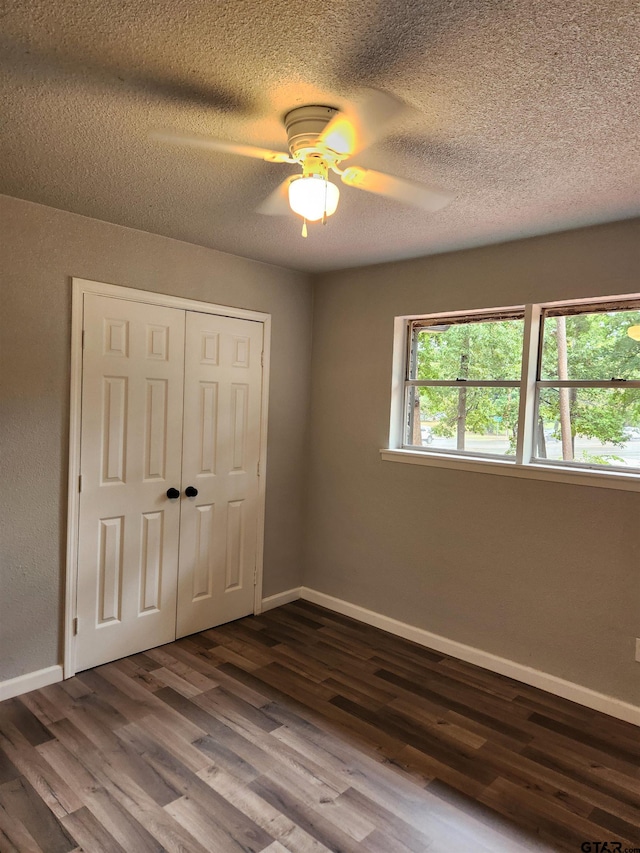 unfurnished bedroom with a textured ceiling, ceiling fan, dark wood-type flooring, and a closet