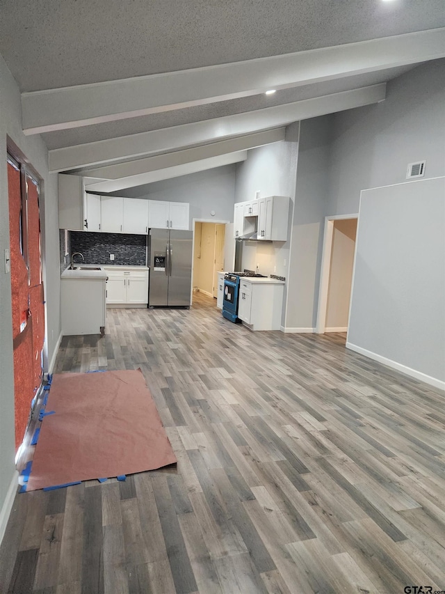 kitchen featuring lofted ceiling with beams, white range with gas stovetop, stainless steel fridge, decorative backsplash, and white cabinets