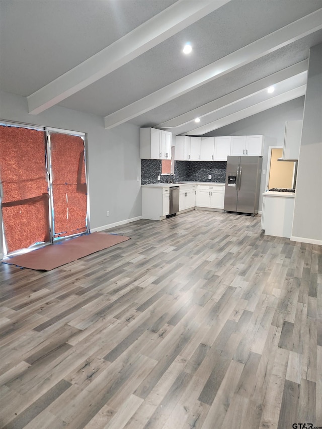 kitchen featuring tasteful backsplash, white cabinetry, lofted ceiling with beams, and appliances with stainless steel finishes