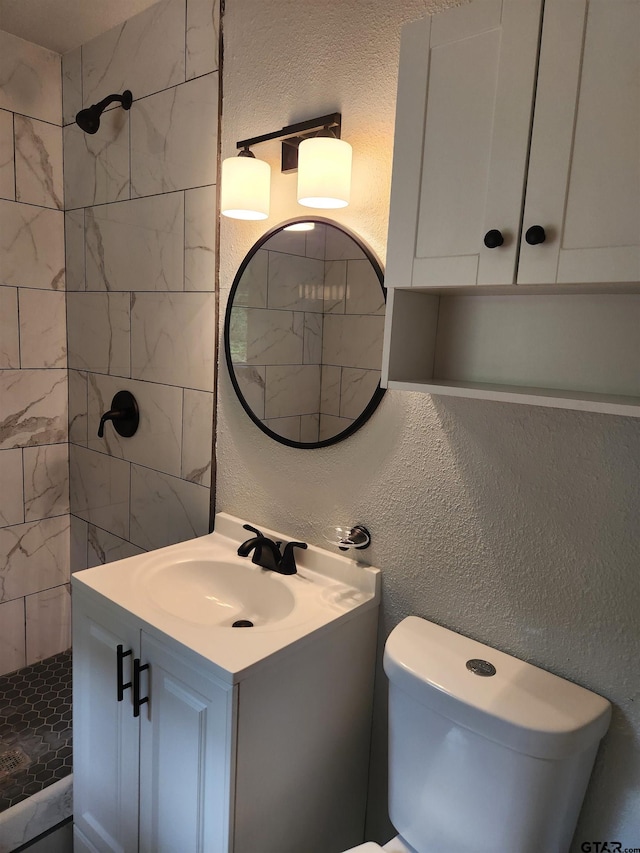 bathroom with tiled shower, vanity, and toilet