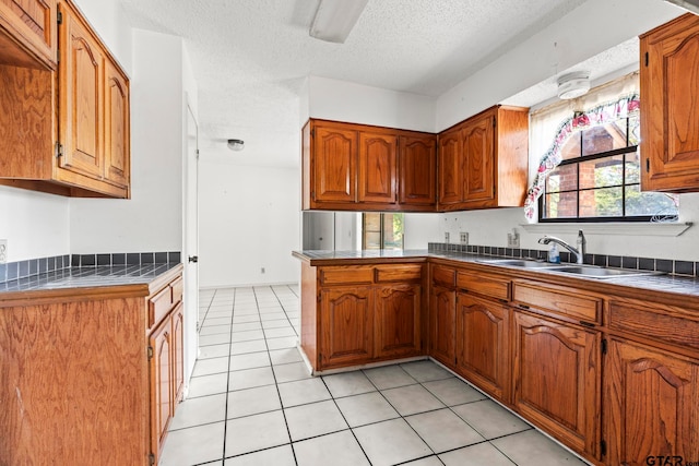 kitchen with tile countertops, sink, kitchen peninsula, a textured ceiling, and light tile patterned floors