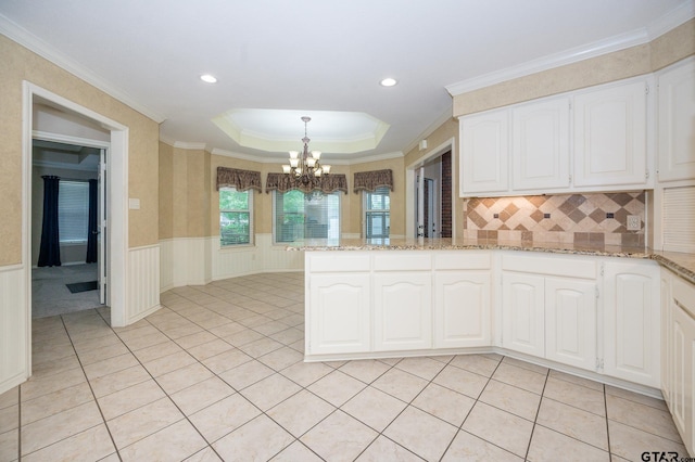 5607 Bostick Dr, Tyler, TX 75707 - kitchen with a chandelier, a peninsula, white cabinets, wainscoting, and backsplash