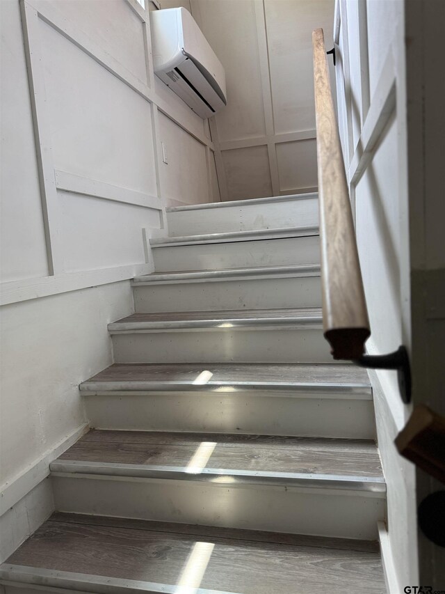 stairs with a wall mounted air conditioner and wood finished floors