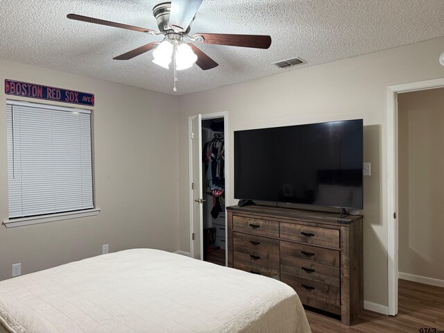 bedroom featuring a spacious closet, visible vents, a textured ceiling, and wood finished floors