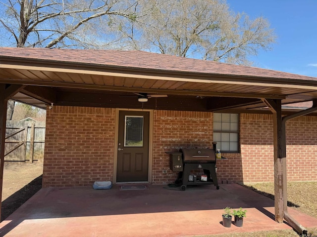 view of exterior entry featuring brick siding, a shingled roof, and fence