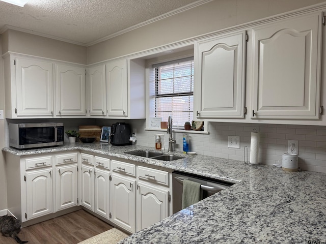 kitchen with stainless steel microwave, dark wood-type flooring, dishwashing machine, white cabinetry, and a sink