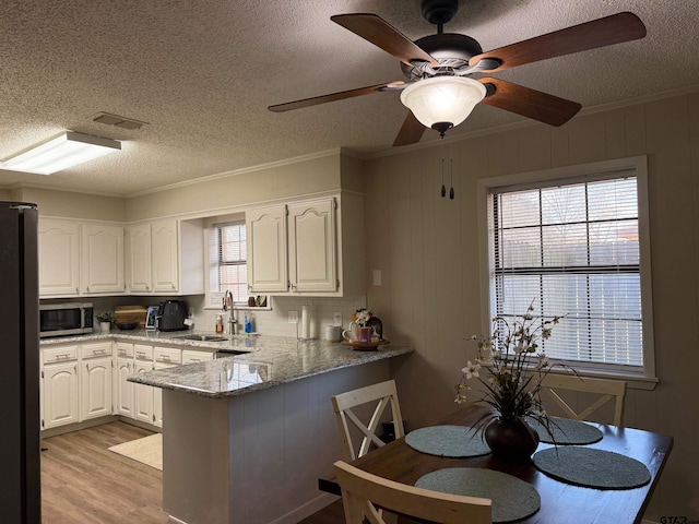 kitchen featuring a sink, stainless steel microwave, freestanding refrigerator, white cabinetry, and a peninsula