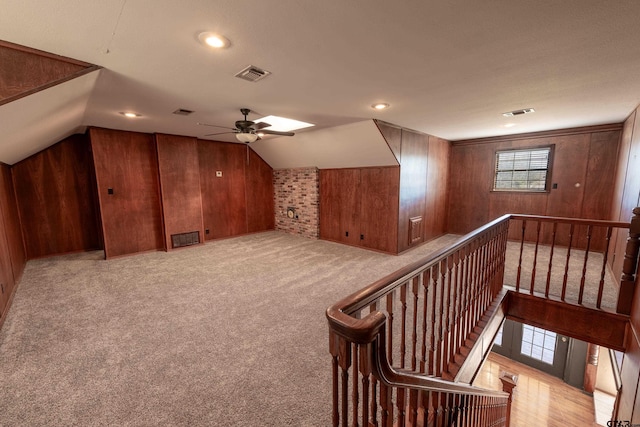 additional living space featuring light carpet, vaulted ceiling, ceiling fan, and wooden walls