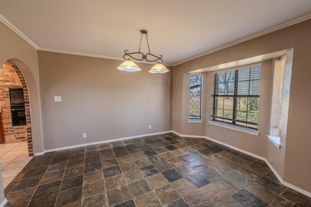 empty room with baseboards, arched walkways, crown molding, and stone finish floor