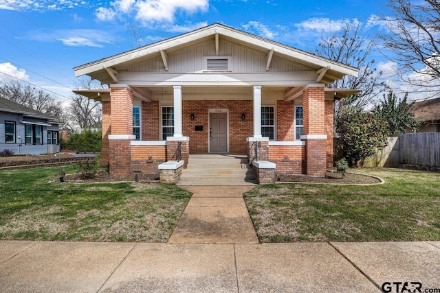 view of front of home with a porch, fence, a front lawn, and brick siding