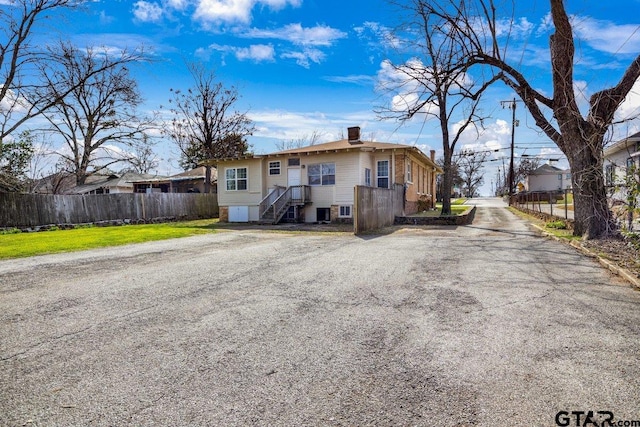 view of front of property featuring driveway, a chimney, and fence