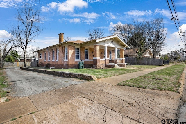 view of front facade featuring covered porch, brick siding, fence, a front lawn, and a chimney