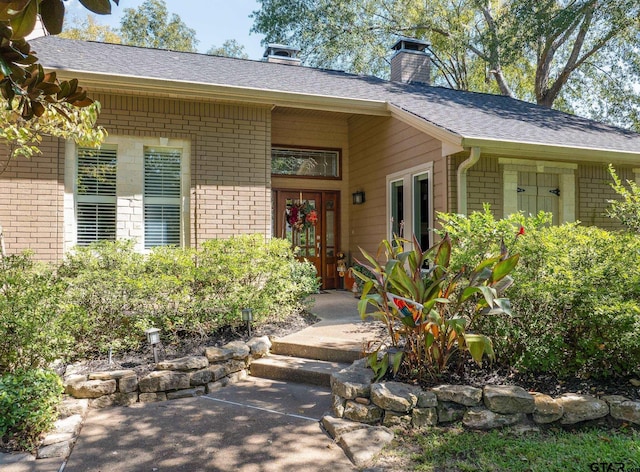 doorway to property featuring brick siding, roof with shingles, and a chimney