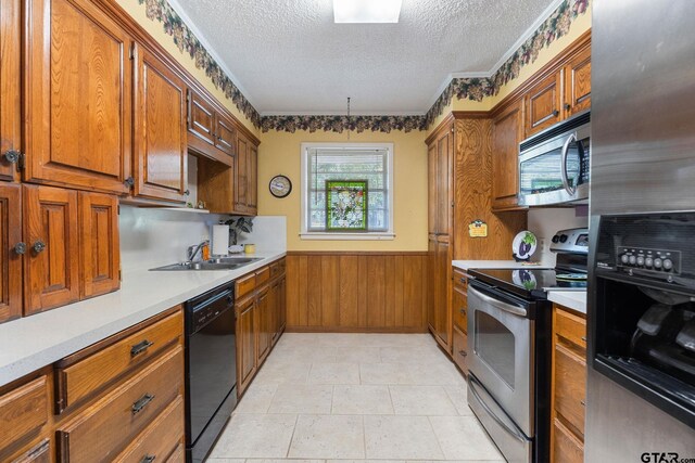 kitchen featuring a textured ceiling, wooden walls, sink, and stainless steel appliances