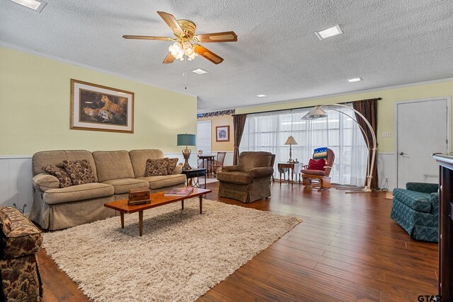 living room featuring dark wood-type flooring, ornamental molding, a textured ceiling, and ceiling fan