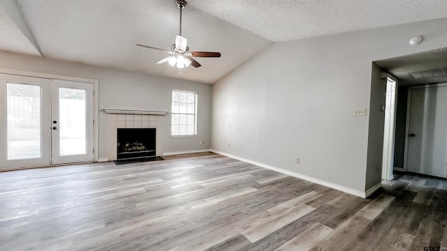 unfurnished living room with french doors, ceiling fan, wood-type flooring, a fireplace, and lofted ceiling