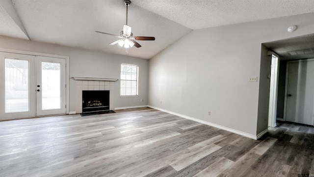 unfurnished living room featuring ceiling fan, french doors, hardwood / wood-style floors, vaulted ceiling, and a fireplace