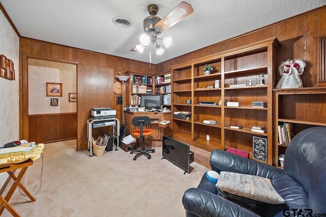 carpeted office space with ceiling fan, ornamental molding, a textured ceiling, and wood walls