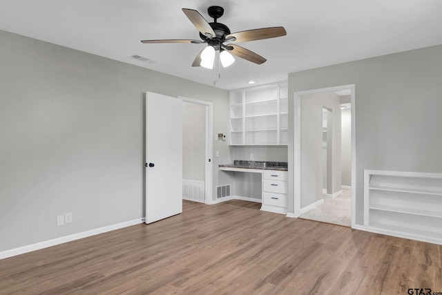 unfurnished bedroom with ceiling fan, built in desk, and light hardwood / wood-style flooring