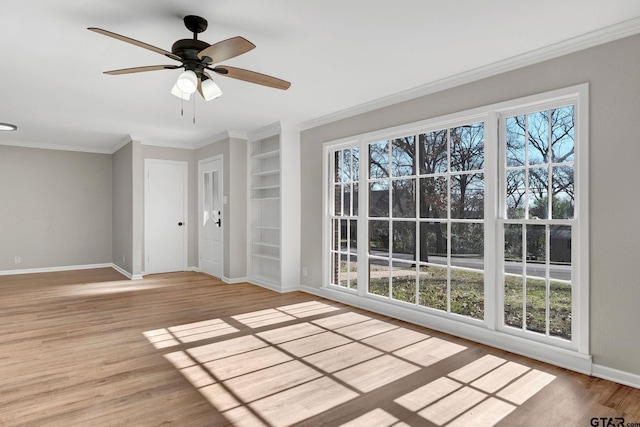 empty room with ceiling fan, built in shelves, ornamental molding, and light hardwood / wood-style floors