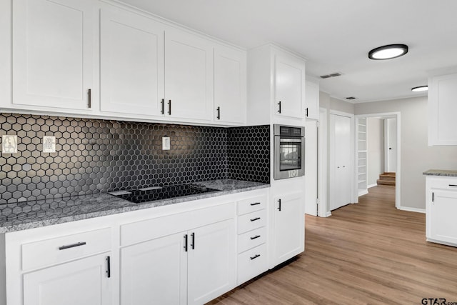 kitchen featuring white cabinetry, stainless steel oven, light hardwood / wood-style floors, and tasteful backsplash