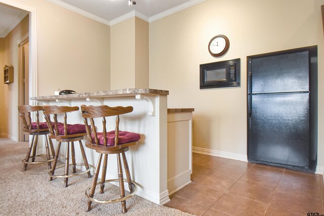 1860 Holcomb Cir, Tyler, TX 75703 - kitchen featuring a kitchen bar, ornamental molding, freestanding refrigerator, tile patterned flooring, and baseboards